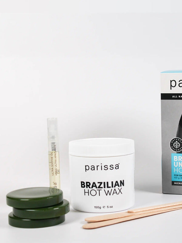 Three dark green wax discs stacked beside a white Parissa Brazilian Hot Wax jar, a slim tube and wooden spatulas, with the turquoise-panel box partly visible behind.