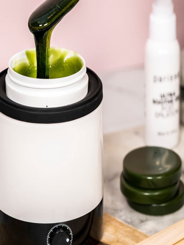 Dark green Parissa Brazilian and Underarm Hot Wax being lifted from a white wax warmer with a wooden applicator.