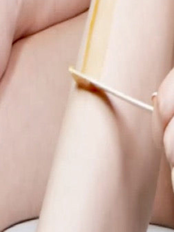 Close-up of Parissa Warm Wax being spread along a lower leg with a wooden applicator while the skin is supported by the other hand.