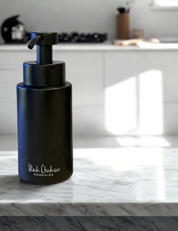 Matte black PureFoam pump dispenser standing on a white marble kitchen counter, with white cabinets and a cooktop in the background.