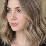 Woman modelling Radico Ash Blonde hair colour, with a centre part and shoulder-length loose waves in a muted beige-brown shade with lighter strands framing her face.