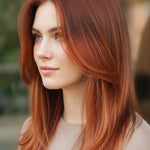 Woman with long, layered copper-red hair and a centre part, shown outdoors with a small label beneath identifying the shade as Auburn Red.