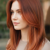 Woman with long, layered copper-red hair and a centre part, shown outdoors with a small label beneath identifying the shade as Auburn Red.