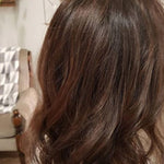 Rear view of dark brown hair falling to the shoulders in broad, loose curls, with a small label beneath identifying the shade as Brown.