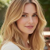 Woman outdoors with shoulder-length pale golden-blonde waves and darker roots, with a small label beneath identifying the shade as Champagne Blonde.