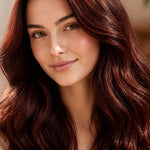 Woman modelling Radico Mahogany hair colour, with long, glossy deep reddish-brown waves and brighter red strands catching the light.