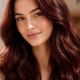 Woman modelling Radico Mahogany hair colour, with long, glossy deep reddish-brown waves and brighter red strands catching the light.