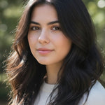 Woman outdoors with centre-parted black hair falling in loose waves around her shoulders, with a small label beneath identifying the shade as Soft Black.