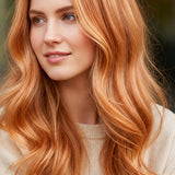 Woman modelling Radico Strawberry Blonde hair colour, with a centre part and long, loose peach-copper waves with pale golden strands around her face.