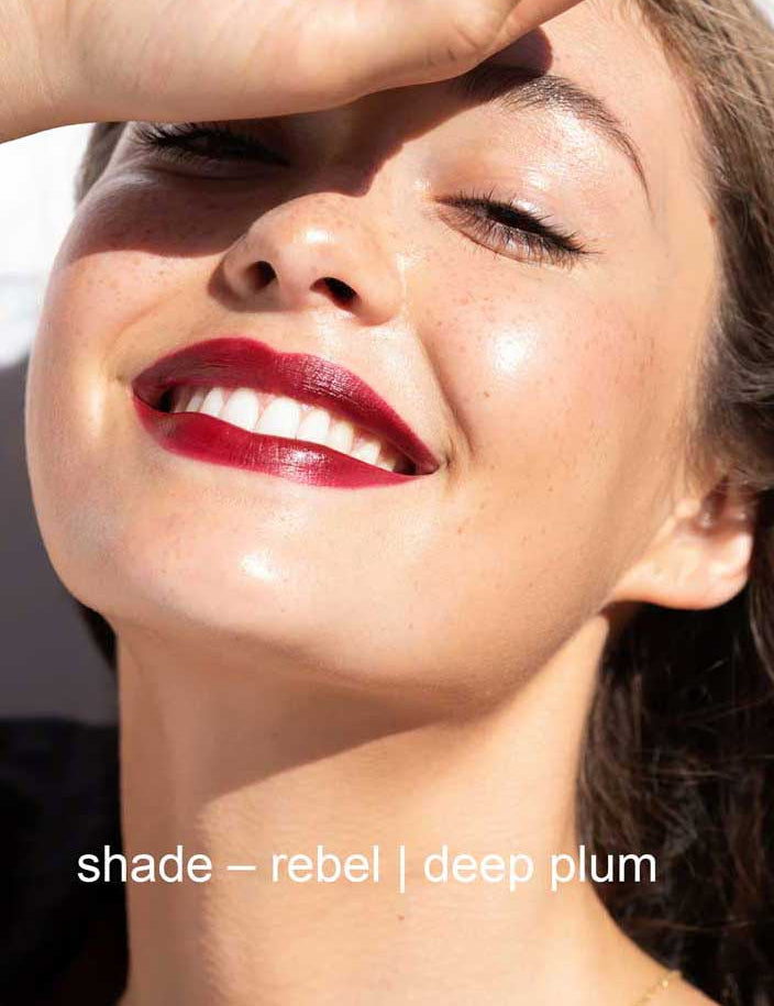 Close-up of a woman's face with red lipstick and text 'shade - rebel | deep plum'.