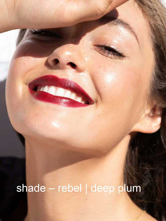 Close-up of a woman's face with red lipstick and text 'shade - rebel | deep plum'.