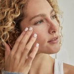 Woman pressing a translucent crescent-shaped Revive My Eyes patch beneath her eye with her fingertips.