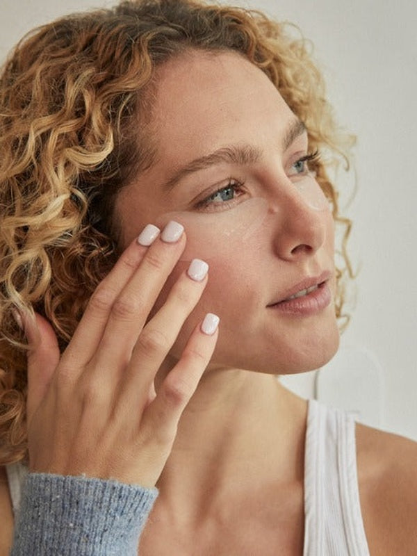 Woman pressing a translucent crescent-shaped Revive My Eyes patch beneath her eye with her fingertips.