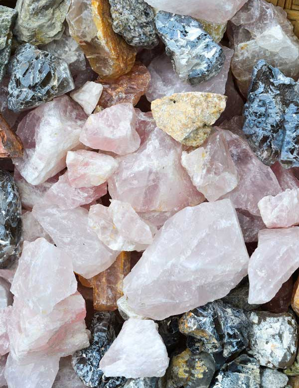 A close-up of assorted rough stones, like large rose quartz crystals—often linked to glowing skin—plus dark and tan rocks. Stones differ in size and texture, echoing the smoothing effects of Acure Resurfacing Overnight Glycolic Treatment.