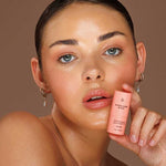 Model wearing Avocado Zinc SPF50 Natural Lip & Cheek Tint in Rose and holding the tint beside her face.