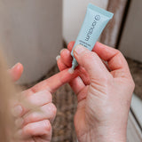 Sanctum Energising Eye Gel tube opened and held in both hands during a skincare routine.