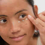 Woman applying Sanctum Firming Eye Balm beneath her eye with a fingertip.