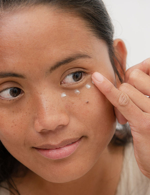 Woman applying Sanctum Firming Eye Balm beneath her eye with a fingertip.