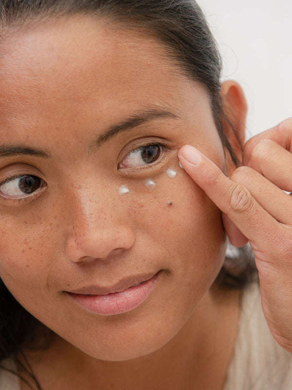 Woman applying Sanctum Firming Eye Balm beneath her eye with a fingertip.
