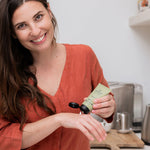 Woman applying Sanctum Hand and Nail Repair cream to her hands in a bright home setting.