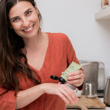 Woman applying Sanctum Hand and Nail Repair cream to her hands in a bright home setting.
