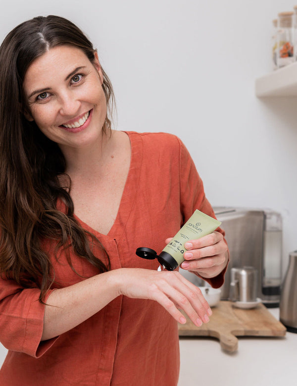 Woman applying Sanctum Hand and Nail Repair cream to her hands in a bright home setting.