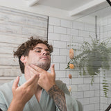 Man washing his face with Sanctum Men's Facial Wash while looking into a bathroom mirror.