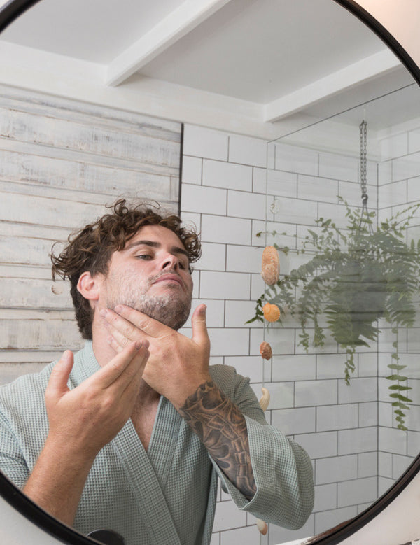 Man washing his face with Sanctum Men's Facial Wash while looking into a bathroom mirror.