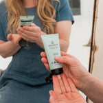 Woman dispensing Sanctum Moisture Balance moisturiser from a pale tube into her open palm in soft natural light.