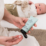 Sanctum Moisture Replenish tube dispensed into a palm beside a resting baby.
