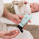 Sanctum Moisture Replenish tube dispensed into a palm beside a resting baby.