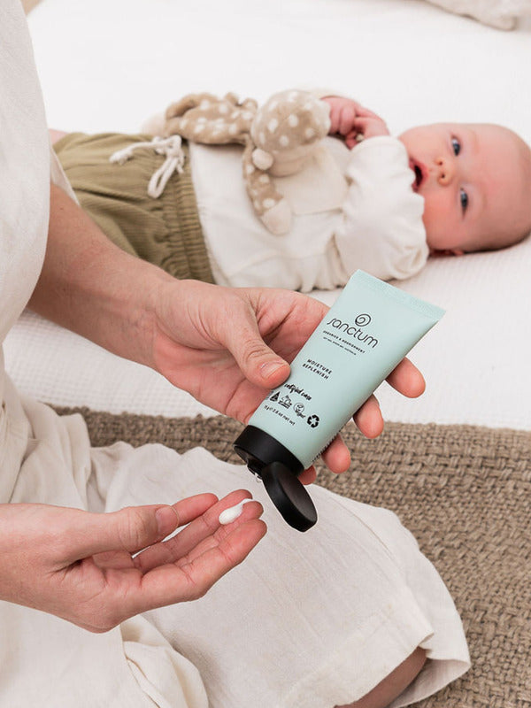 Sanctum Moisture Replenish tube dispensed into a palm beside a resting baby.
