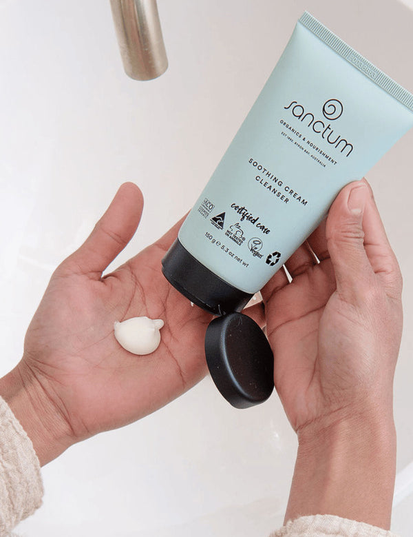 Hands dispensing Sanctum Soothing Cream Cleanser from the tube during a skincare routine.
