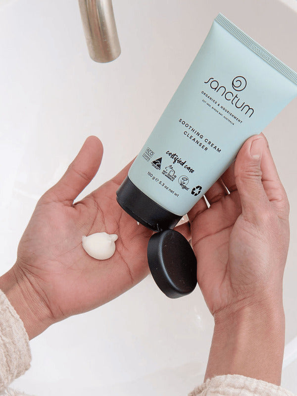 Hands dispensing Sanctum Soothing Cream Cleanser from the tube during a skincare routine.