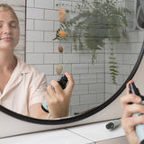 Woman spraying Sanctum Tone & Refresh Mist toward her face while looking into a bathroom mirror.