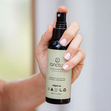 Hand holding Sanctum Women's Deodorant Spray upright with the front label facing the camera.