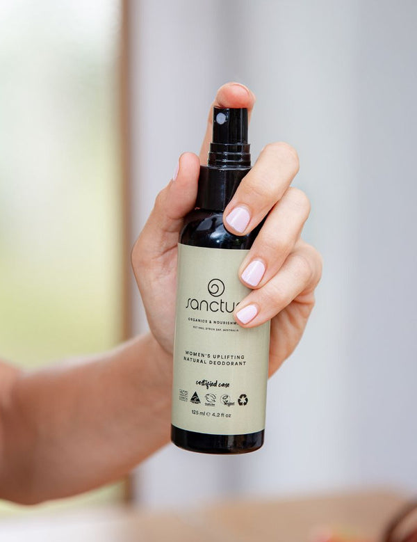 Hand holding Sanctum Women's Deodorant Spray upright with the front label facing the camera.