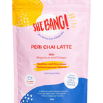 Pink resealable She BANG! Peri Chai Latte pouch with a bright yellow patch at the upper left, a curved blue panel along the bottom, scattered white dots and bold red lettering.