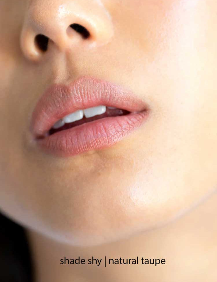 Close-up of lips wearing Ere Perez Acai Lip Pencils 1.1g in shade Shy, a natural taupe. Hydrating formula delivers smooth, moisturized lips. Text at bottom: shade shy | natural taupe.