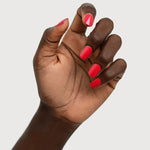 A deep-brown hand with fingers loosely curled to display glossy coral-red nails painted in Sienna Byron Bay Dance.