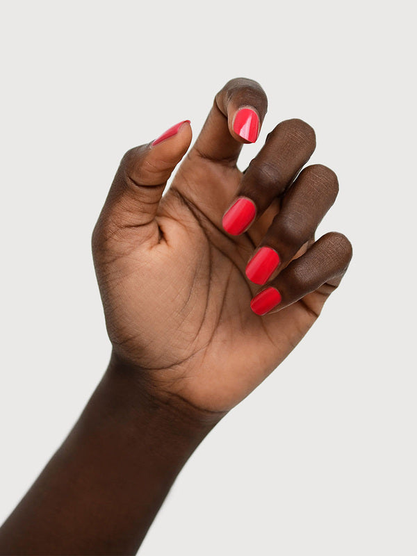 A deep-brown hand with fingers loosely curled to display glossy coral-red nails painted in Sienna Byron Bay Dance.
