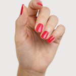 A light-skinned hand with fingers loosely curled to display glossy coral-red nails painted in Sienna Byron Bay Dance.