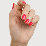 A light-skinned hand with fingers loosely curled to display glossy coral-red nails painted in Sienna Byron Bay Dance.