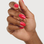 A medium-brown hand with fingers loosely curled to display rounded, glossy coral-red nails painted in Sienna Byron Bay Dance.