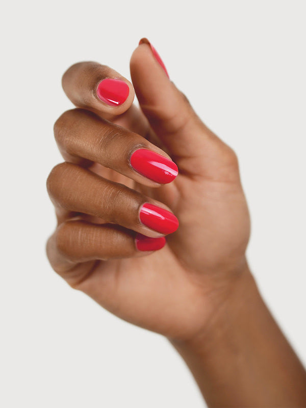 A medium-brown hand with fingers loosely curled to display rounded, glossy coral-red nails painted in Sienna Byron Bay Dance.