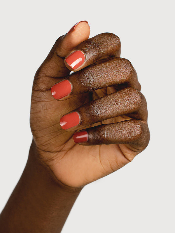 A deep-brown hand with fingers loosely curled to display glossy terracotta-red nails painted in Sienna Byron Bay Life.