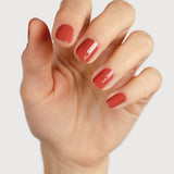 A light-skinned hand with fingers loosely curled to display glossy terracotta-red nails painted in Sienna Byron Bay Life.