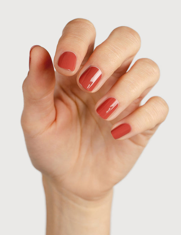A light-skinned hand with fingers loosely curled to display glossy terracotta-red nails painted in Sienna Byron Bay Life.