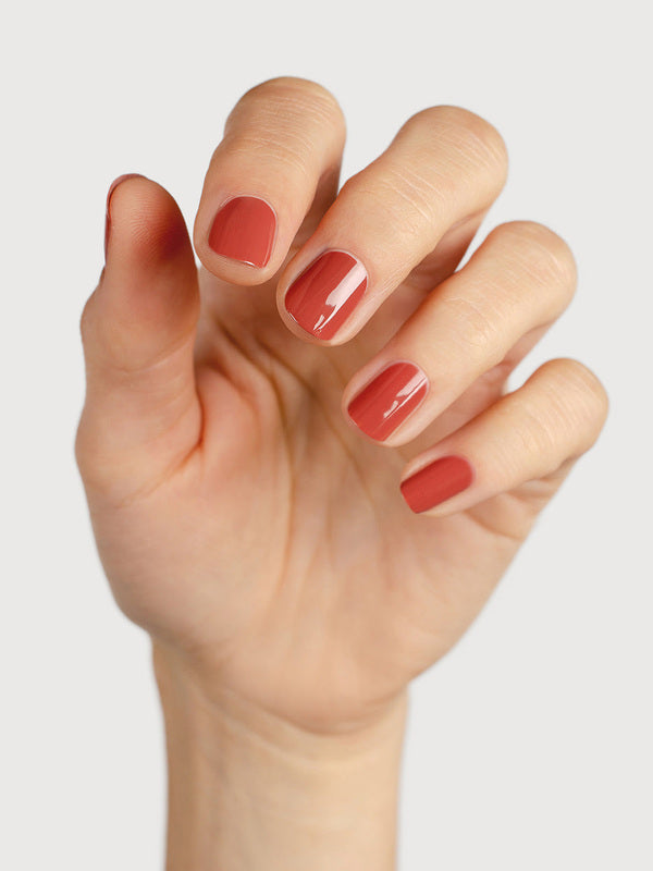 A light-skinned hand with fingers loosely curled to display glossy terracotta-red nails painted in Sienna Byron Bay Life.