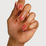 A medium-brown hand with fingers loosely curled to display glossy terracotta-red nails painted in Sienna Byron Bay Life.
